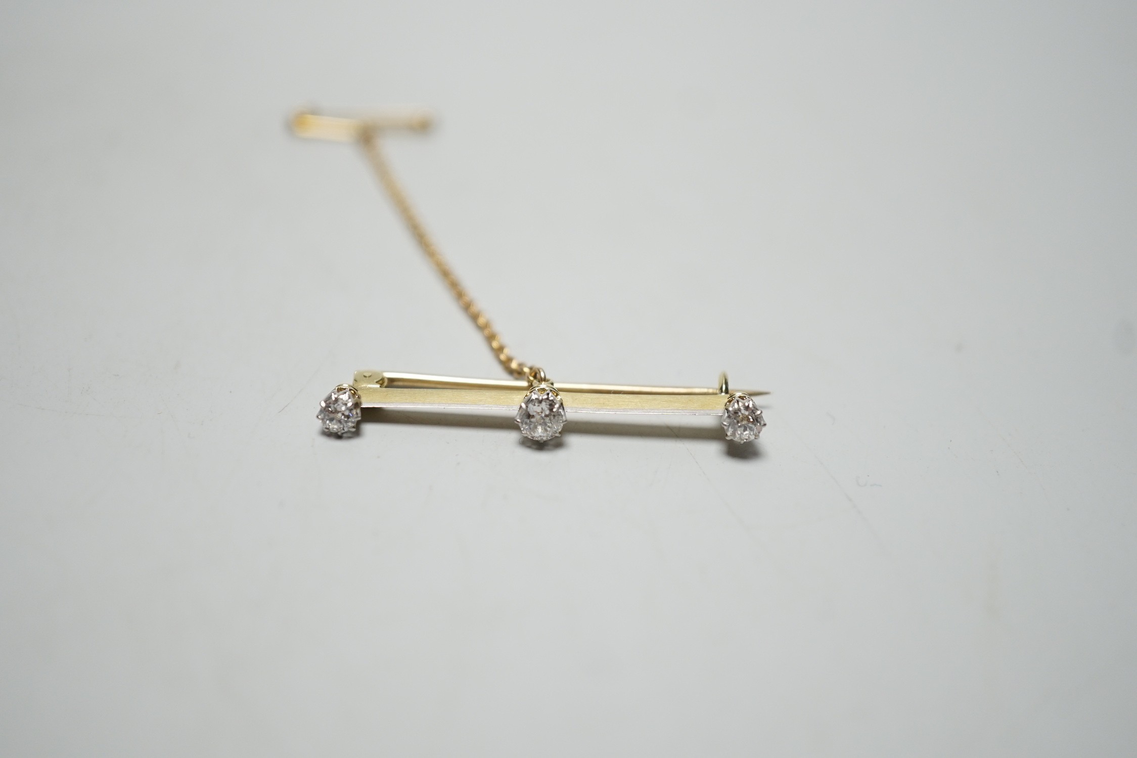 A yellow metal and three stone diamond set bar brooch, 36mm, gross weight 2.8 grams.